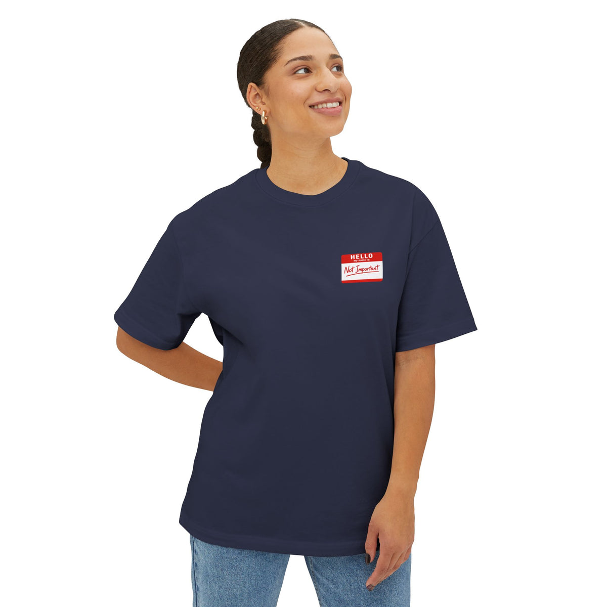 A woman wearing a navy blue crewneck t-shirt with a small red and white name tag graphic on the left chest, paired with light blue jeans, set against a plain white background.